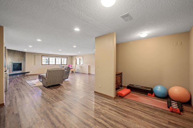 living room featuring recessed lighting, a large fireplace, a textured ceiling, wood finished floors, and baseboards