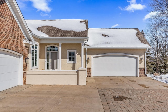 view of front of property featuring a garage, brick siding, roof with shingles, decorative driveway, and stucco siding