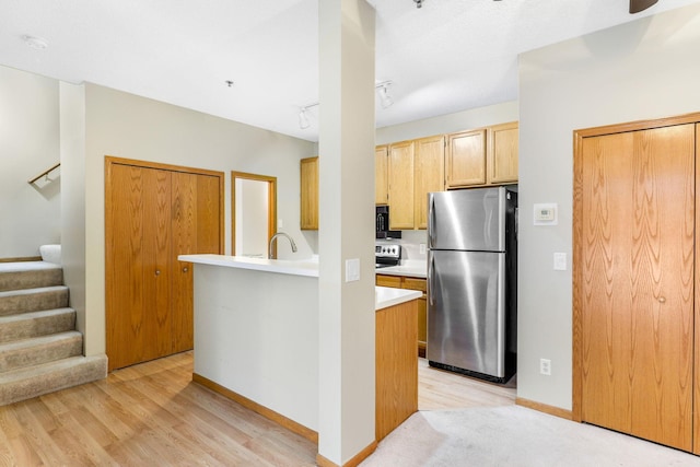 kitchen featuring stainless steel appliances, sink, kitchen peninsula, light hardwood / wood-style flooring, and light brown cabinetry