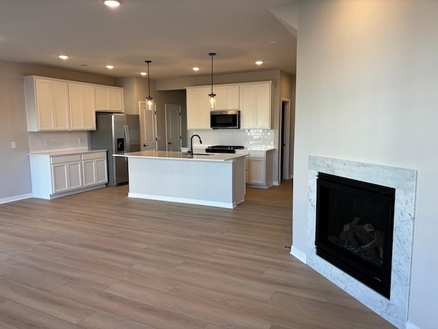 kitchen featuring light wood finished floors, stainless steel appliances, recessed lighting, a high end fireplace, and white cabinets