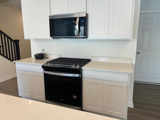 kitchen with dark wood-type flooring, stainless steel microwave, black gas stove, and white cabinetry