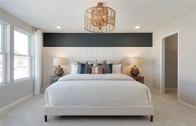 bedroom featuring light carpet, a chandelier, a walk in closet, and wainscoting