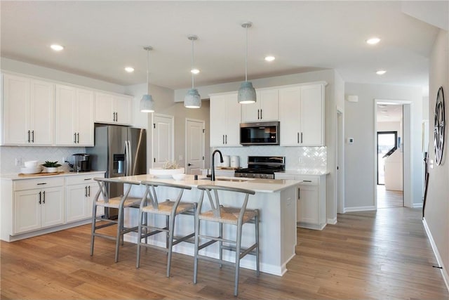 kitchen with a center island with sink, a breakfast bar area, stainless steel appliances, a sink, and light wood-type flooring