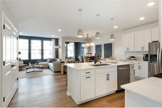 kitchen with stainless steel appliances, white cabinets, a sink, and a center island with sink