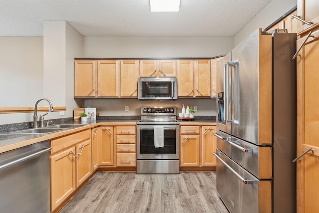 kitchen with light wood-type flooring, appliances with stainless steel finishes, sink, and a textured ceiling