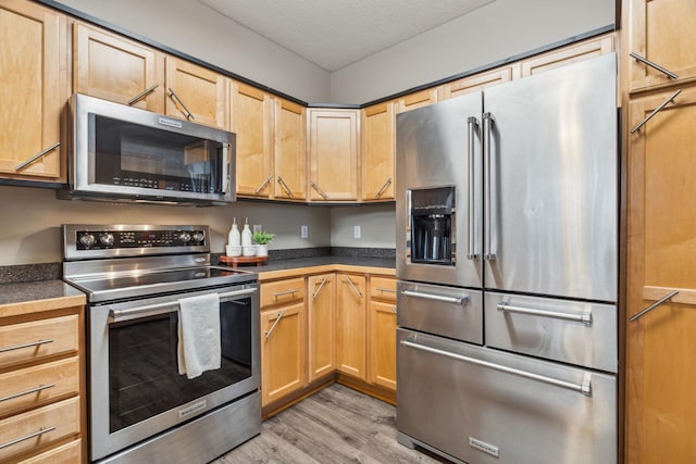 kitchen with a textured ceiling, stainless steel appliances, and light hardwood / wood-style floors