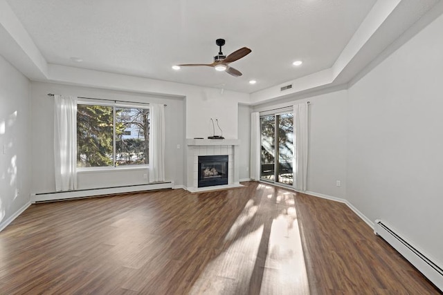 unfurnished living room with dark wood-type flooring, a wealth of natural light, and a baseboard heating unit