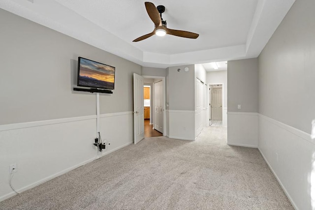 unfurnished bedroom featuring a raised ceiling, ceiling fan, and carpet flooring