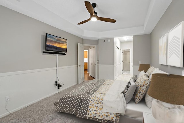 bedroom with a tray ceiling, ensuite bathroom, ceiling fan, and carpet flooring