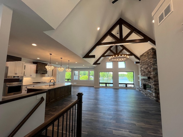 living room featuring dark wood-type flooring, sink, a stone fireplace, and an inviting chandelier