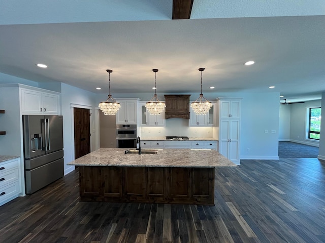 kitchen featuring appliances with stainless steel finishes, decorative light fixtures, sink, white cabinets, and a center island with sink