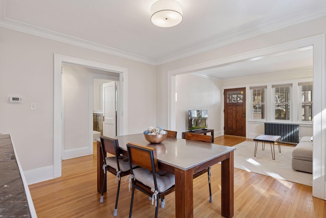 dining space with crown molding, baseboards, radiator heating unit, and light wood-style floors