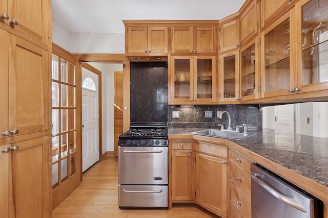 kitchen featuring a sink, stainless steel appliances, glass insert cabinets, tasteful backsplash, and light wood-type flooring