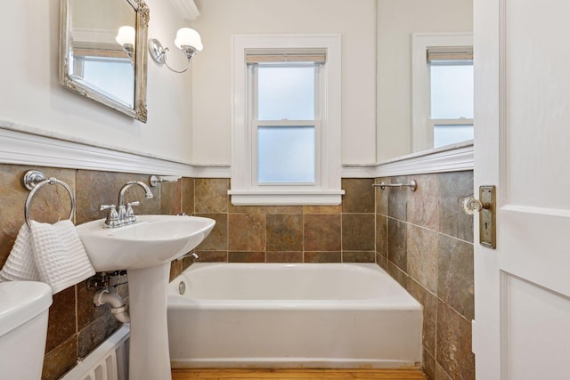 full bath featuring a wainscoted wall, toilet, tile walls, and a bath