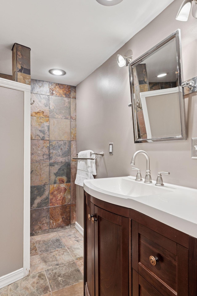 bathroom featuring stone finish floor, a walk in shower, vanity, and baseboards