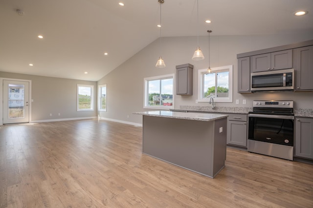 kitchen with a center island, light wood-type flooring, light stone countertops, gray cabinetry, and stainless steel appliances