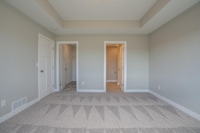 unfurnished bedroom with a tray ceiling, a closet, and light carpet