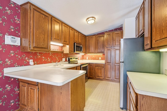 kitchen featuring lofted ceiling, sink, appliances with stainless steel finishes, a textured ceiling, and kitchen peninsula