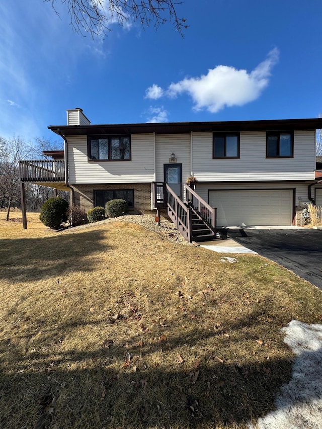 bi-level home with driveway, a garage, a chimney, and a front yard