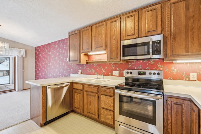 kitchen with stainless steel appliances, brown cabinetry, a peninsula, and wallpapered walls