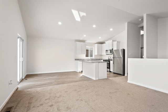 kitchen with light stone countertops, white cabinets, a center island, lofted ceiling, and stainless steel appliances