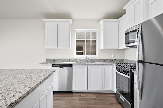 kitchen with stainless steel appliances, dark wood-type flooring, white cabinets, light stone counters, and sink