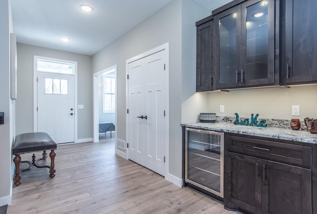 bar with light stone counters, dark brown cabinetry, light hardwood / wood-style flooring, and wine cooler