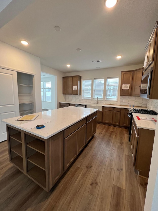 kitchen with appliances with stainless steel finishes, decorative backsplash, dark hardwood / wood-style floors, light stone countertops, and a kitchen island