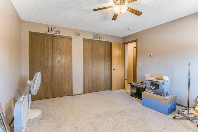 interior space with a textured ceiling, ceiling fan, and two closets