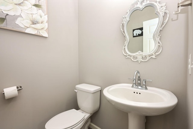 half bath with toilet, baseboards, and a sink