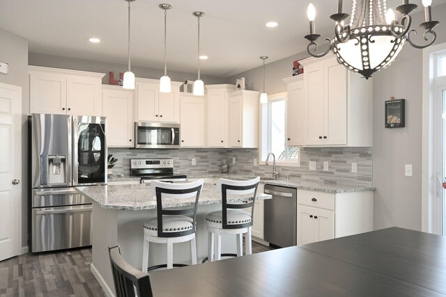 kitchen with tasteful backsplash, decorative light fixtures, a center island, stainless steel appliances, and white cabinetry