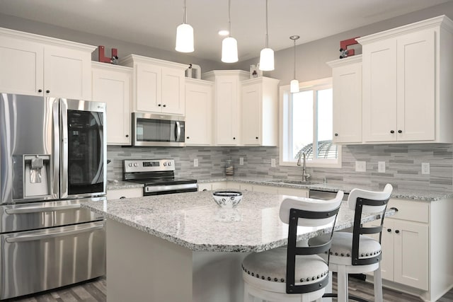 kitchen featuring stainless steel appliances, a sink, white cabinetry, and a center island