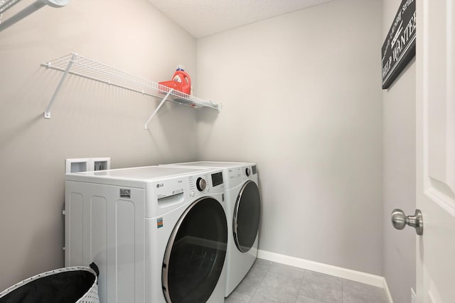 laundry room featuring laundry area, washing machine and dryer, light tile patterned floors, and baseboards