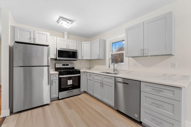 kitchen with gray cabinets, sink, light wood-type flooring, stainless steel appliances, and light stone counters