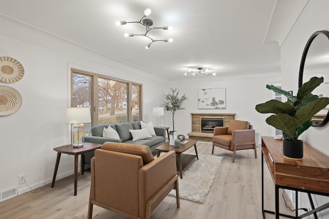 living room with crown molding, a brick fireplace, a notable chandelier, and light hardwood / wood-style flooring