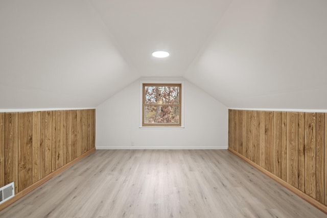 additional living space with light hardwood / wood-style floors, wooden walls, and vaulted ceiling