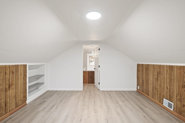 bonus room with vaulted ceiling, built in features, light hardwood / wood-style flooring, and wooden walls