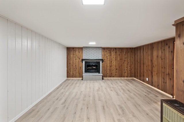 unfurnished living room with a brick fireplace, light wood-type flooring, and wooden walls