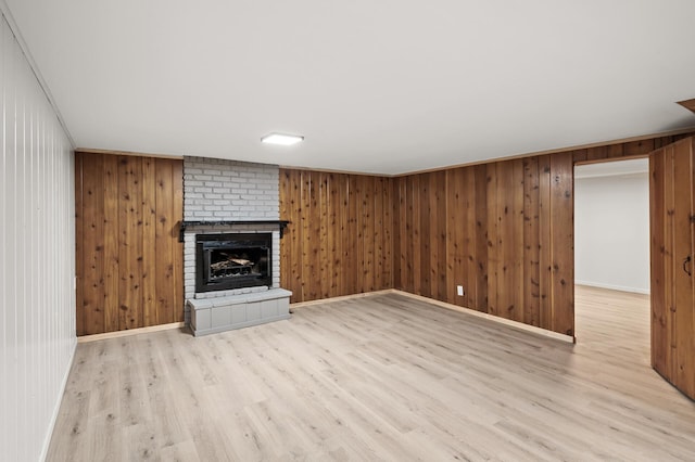 unfurnished living room featuring a fireplace, wooden walls, and light hardwood / wood-style flooring