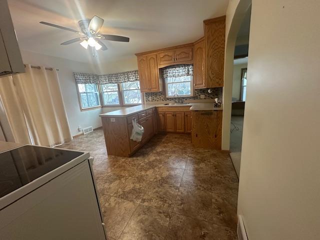 kitchen with white electric range oven, a center island, kitchen peninsula, ceiling fan, and decorative backsplash