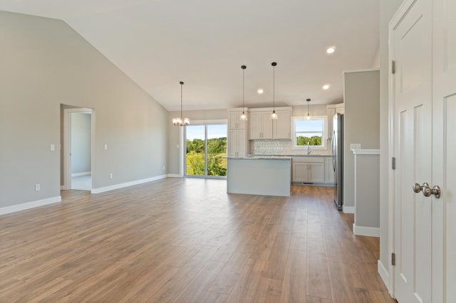 kitchen featuring sink, decorative light fixtures, light hardwood / wood-style flooring, decorative backsplash, and stainless steel refrigerator