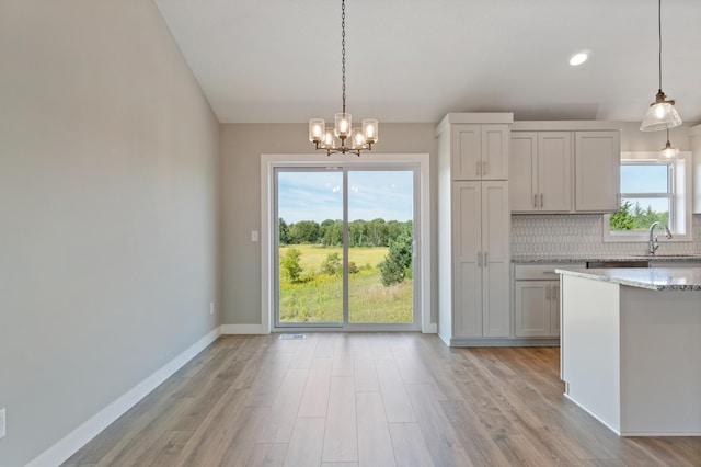 kitchen featuring light stone counters, sink, hanging light fixtures, and decorative backsplash