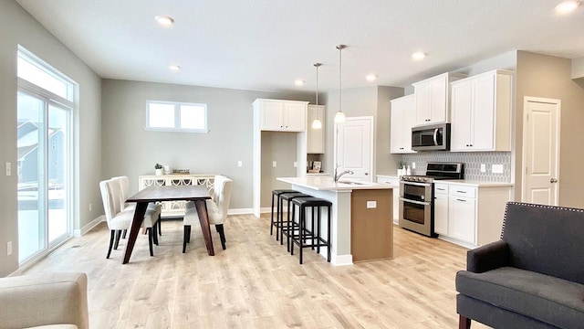 kitchen featuring appliances with stainless steel finishes, decorative light fixtures, white cabinetry, decorative backsplash, and a kitchen island with sink