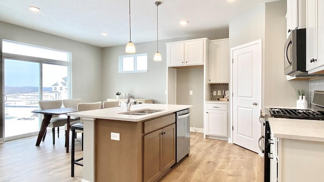 kitchen featuring decorative light fixtures, sink, white cabinetry, a kitchen island with sink, and stainless steel appliances