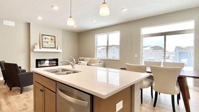 kitchen featuring stainless steel dishwasher, sink, hanging light fixtures, a kitchen island with sink, and a textured ceiling