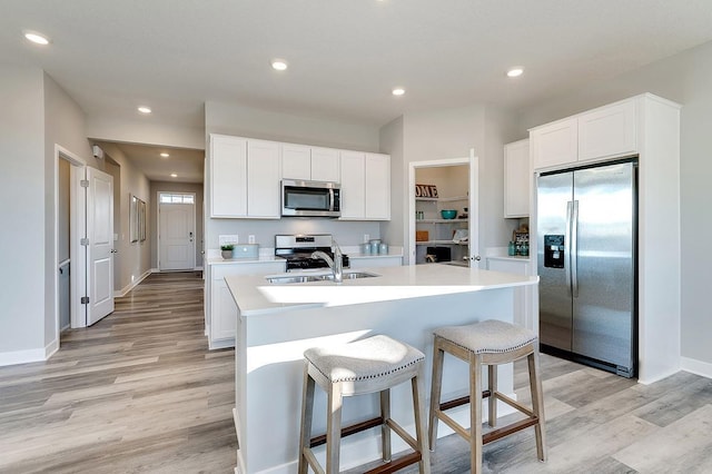 kitchen featuring appliances with stainless steel finishes, white cabinetry, sink, a center island with sink, and light hardwood / wood-style flooring