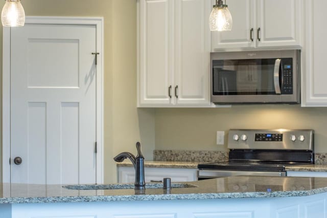 kitchen featuring white cabinetry, hanging light fixtures, light stone counters, and appliances with stainless steel finishes