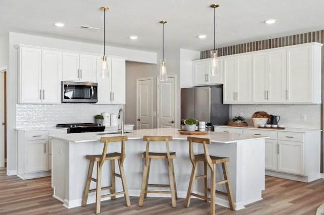 kitchen with decorative light fixtures, appliances with stainless steel finishes, a kitchen island with sink, and white cabinetry