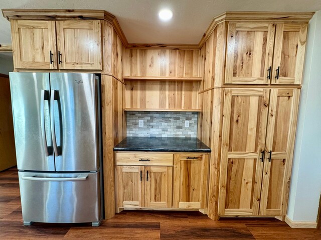 kitchen with light brown cabinetry, dark stone countertops, dark hardwood / wood-style floors, stainless steel fridge, and decorative backsplash