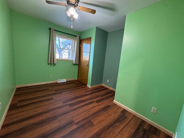 empty room featuring ceiling fan, dark wood-type flooring, and a textured ceiling